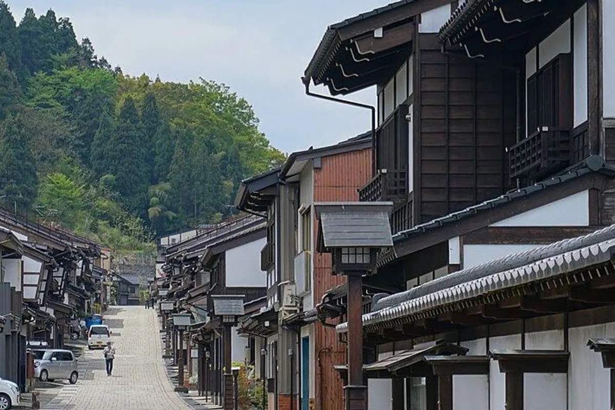 A stone-paved street lined with wooden machiya houses, with a green hill behind.