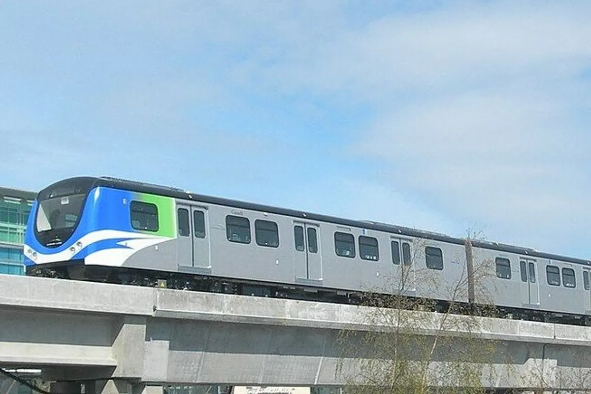 A blue-and-white Canada Line train on the elevated guideway at the airport station.