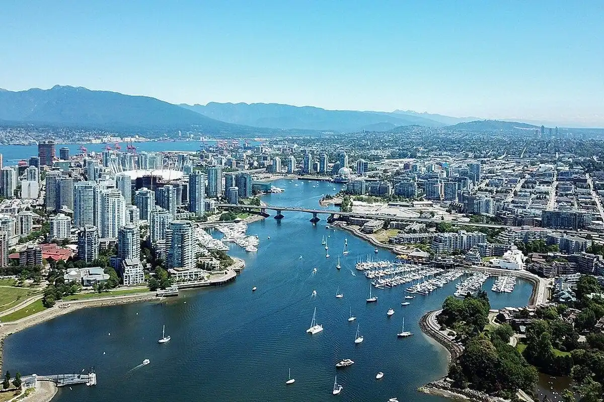 Summer aerial view of sailboats on False Creek, with downtown towers and the North Shore mountains beyond.