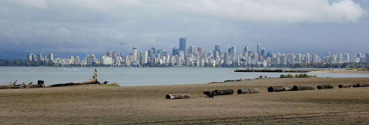 Downtown Vancouver's towers across English Bay on a cloudy day, beyond a driftwood-strewn beach