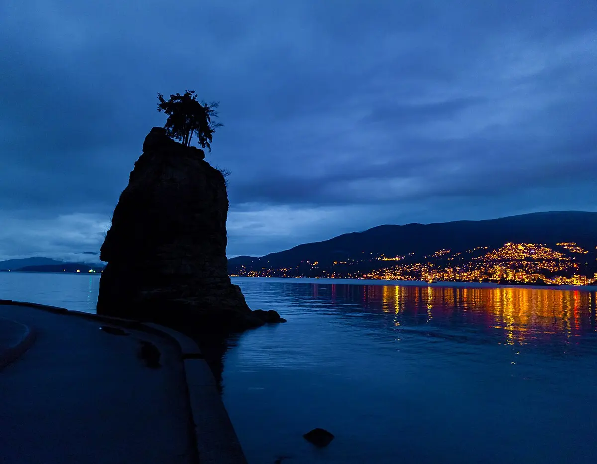 Siwash Rock rising from the water beside the Stanley Park seawall at sunset