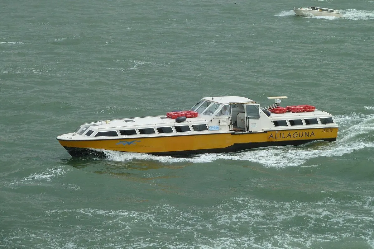 A yellow Alilaguna water bus speeding across the green lagoon, throwing up spray.