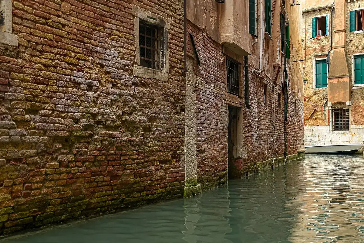 A narrow Venetian canal running between ordinary brick houses with water-level doors and windows.