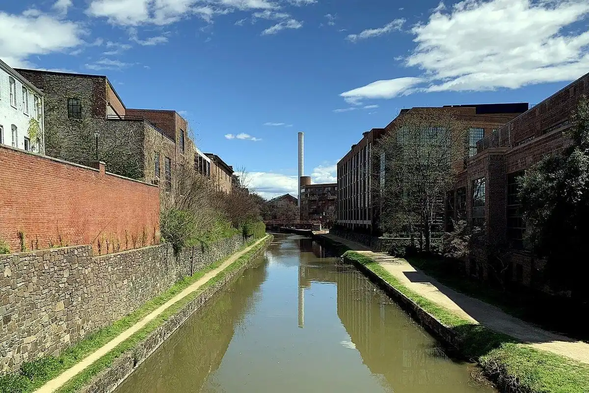 The C&O Canal in Georgetown running between old stone walls and brick buildings, with the towpath alongside, on a sunny spring day.