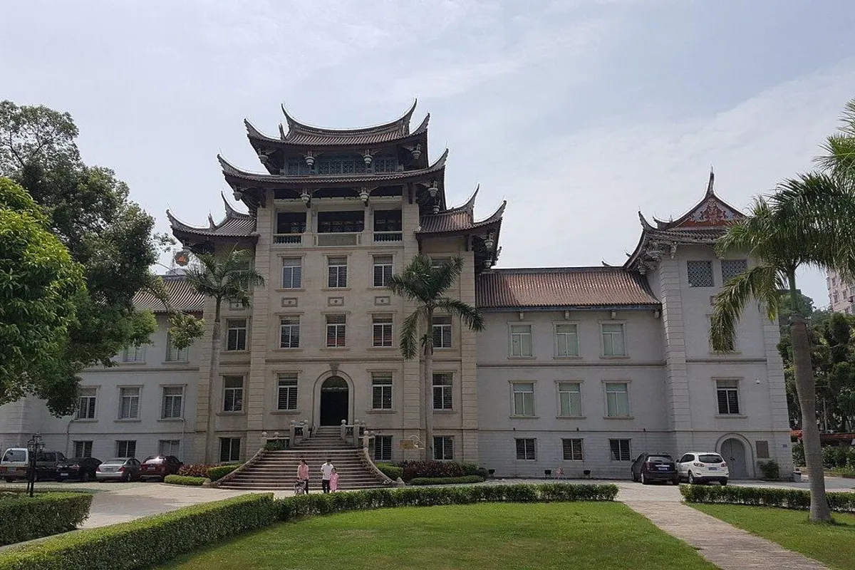 The white stone main building with layered, upturned roofs, a lawn and palm trees in front.
