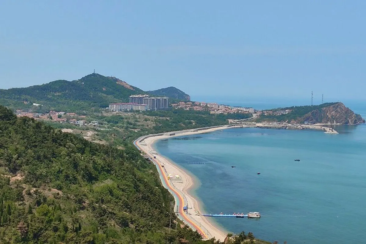 A curving sandy shore and turquoise sea below green hills on South Changshan Island, Changdao.