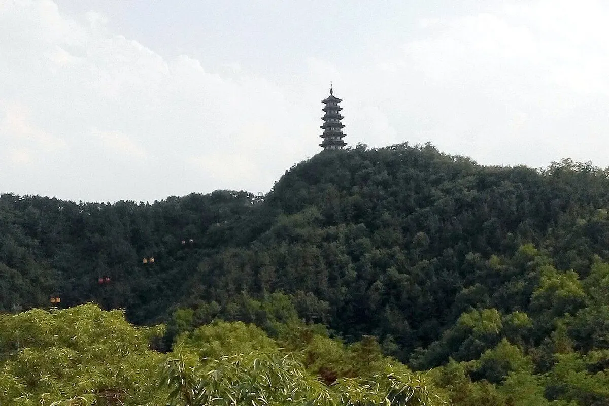 The Sanhe Pagoda rising above a ridge covered in green forest, with small cable cars crossing the slope.