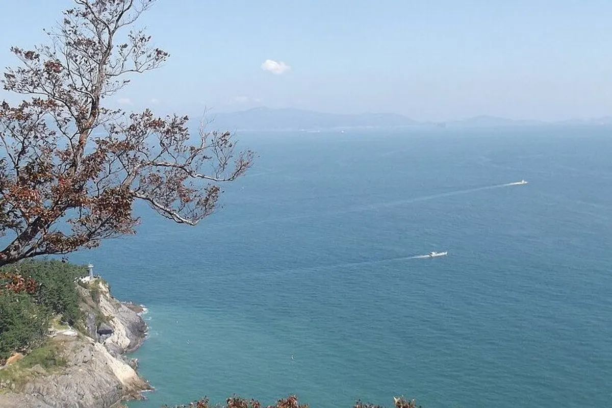 A rocky coast with a small lighthouse and boats on the sea, seen from Hyangiram.