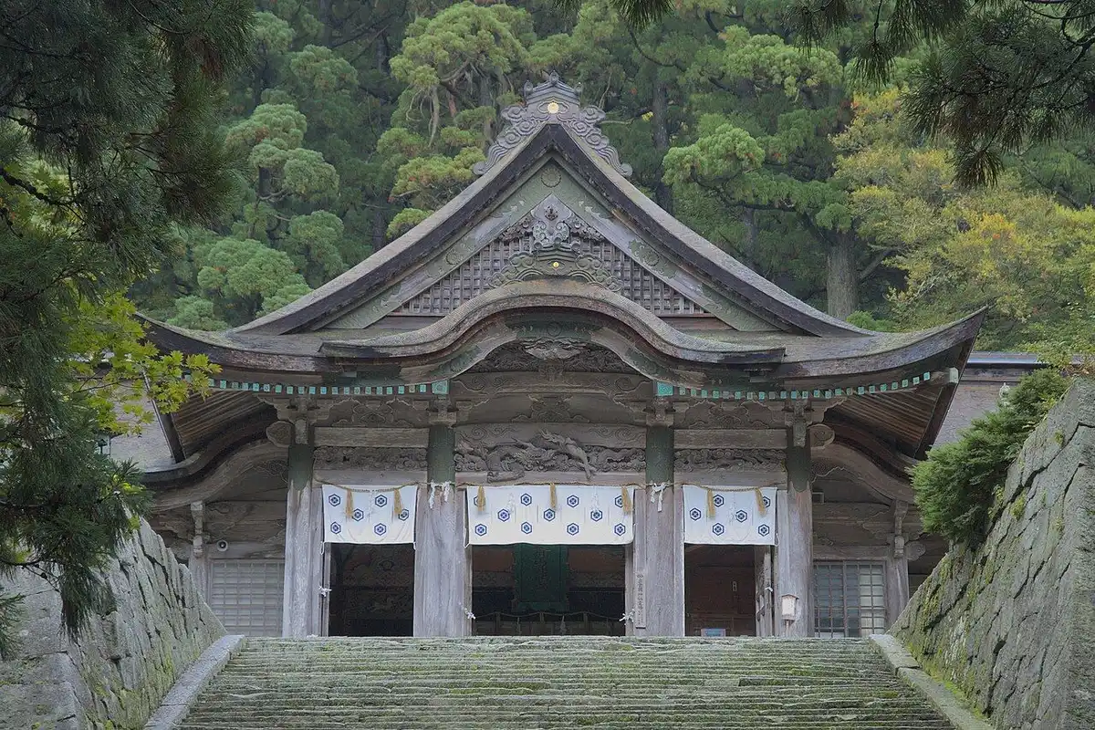 The curved-roof hall of Ogamiyama Shrine Okumiya at the top of stone steps, surrounded by forest.