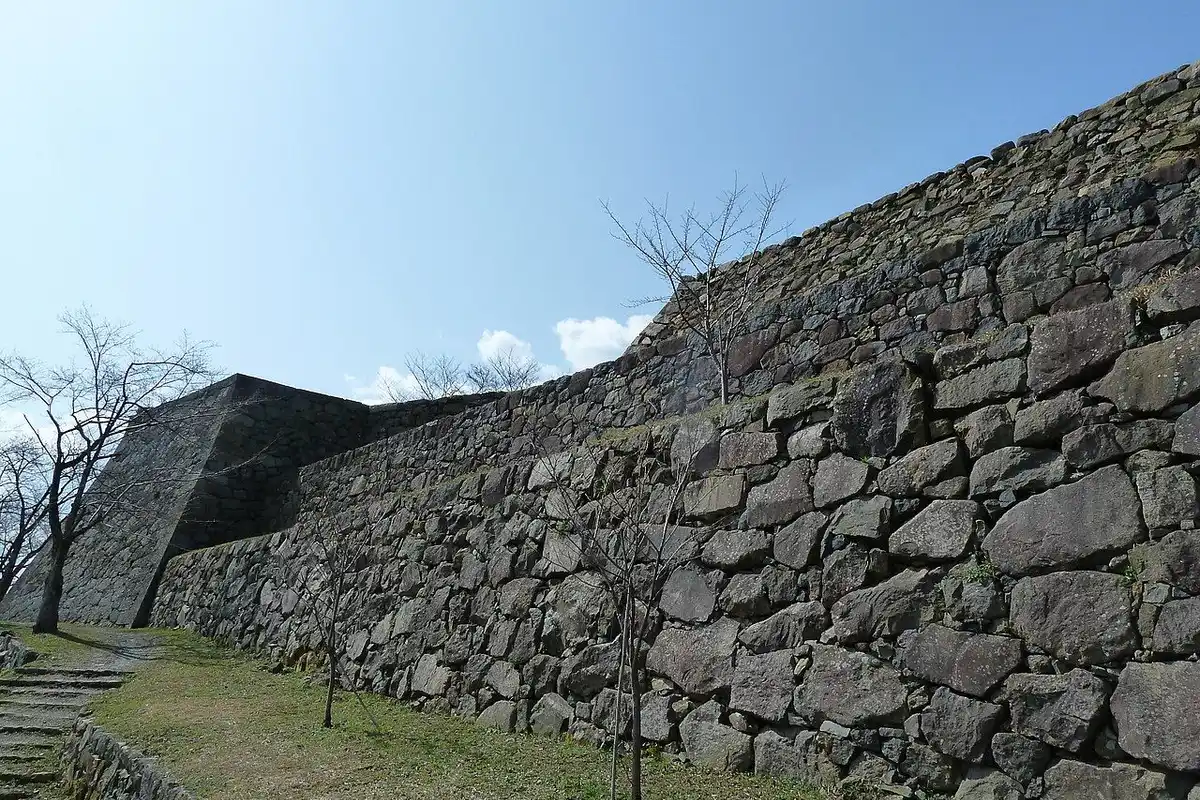 Tall stone walls of the Yonago Castle ruins under a blue sky, with a grassy slope below.