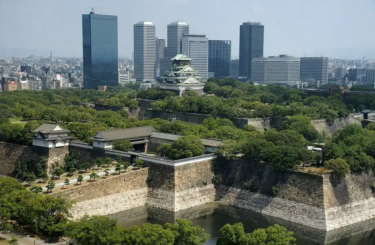 The main keep of Osaka Castle rising above the park greenery with the city skyline behind.
