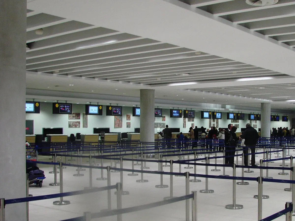 An airport departure hall with queue barriers and a row of check-in counters.
