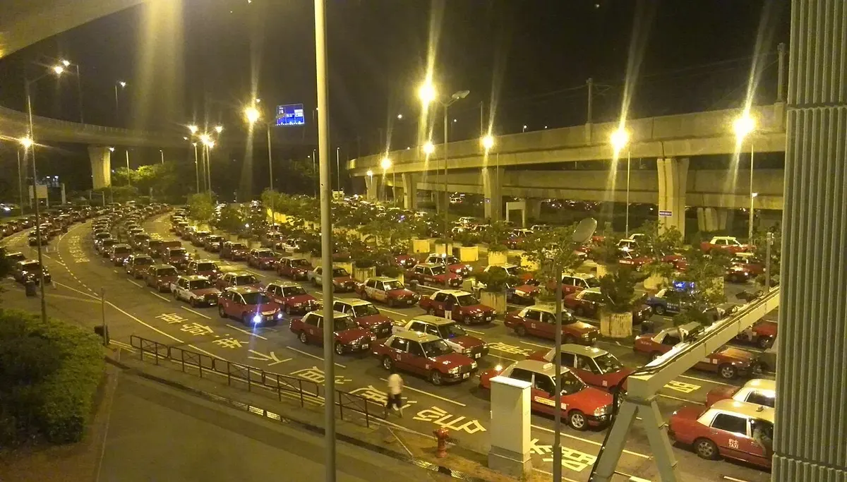 A line of taxis waiting for passengers at an airport taxi rank at night.