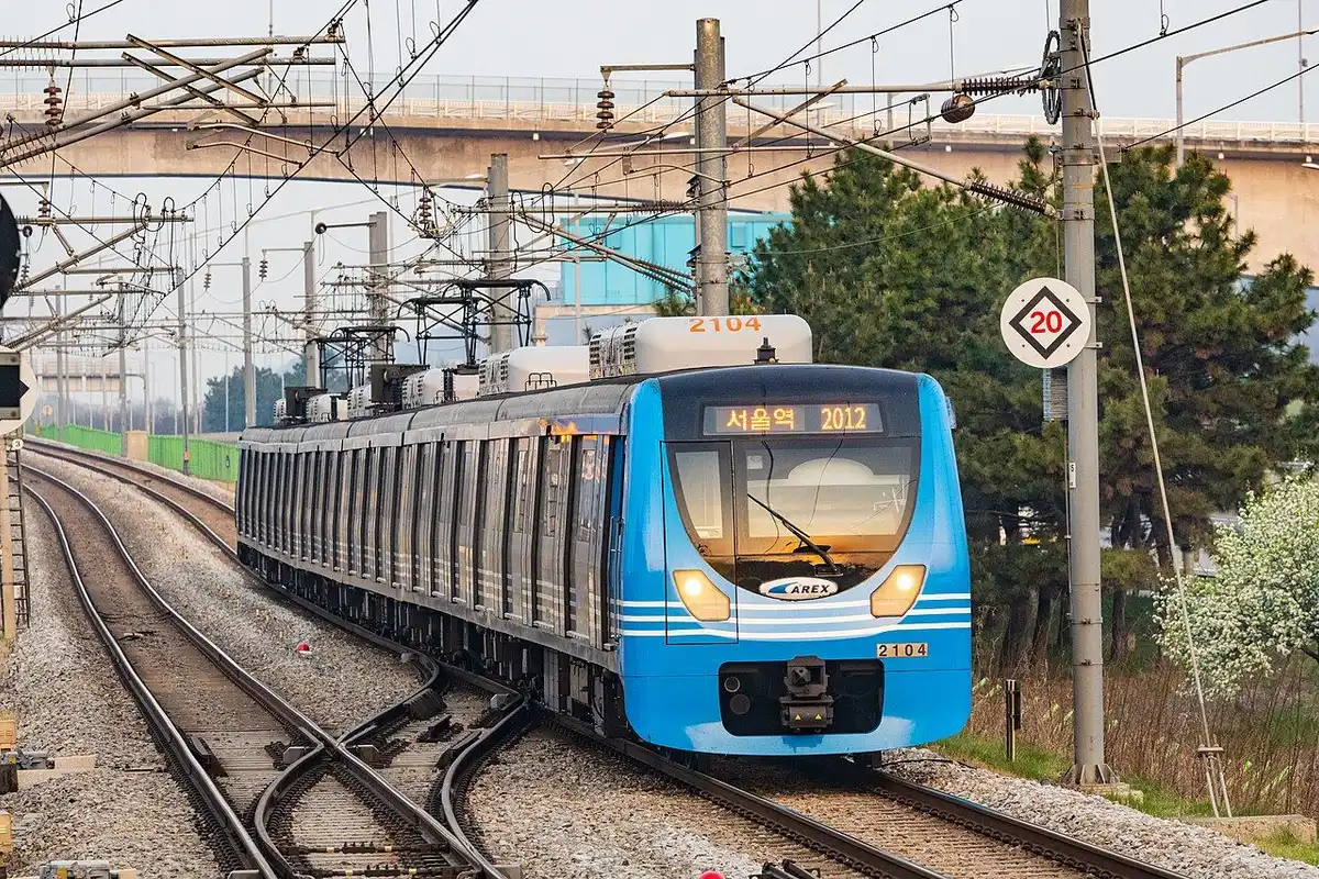 A blue AREX train bound for Seoul Station, with blossoming trees beside the track.