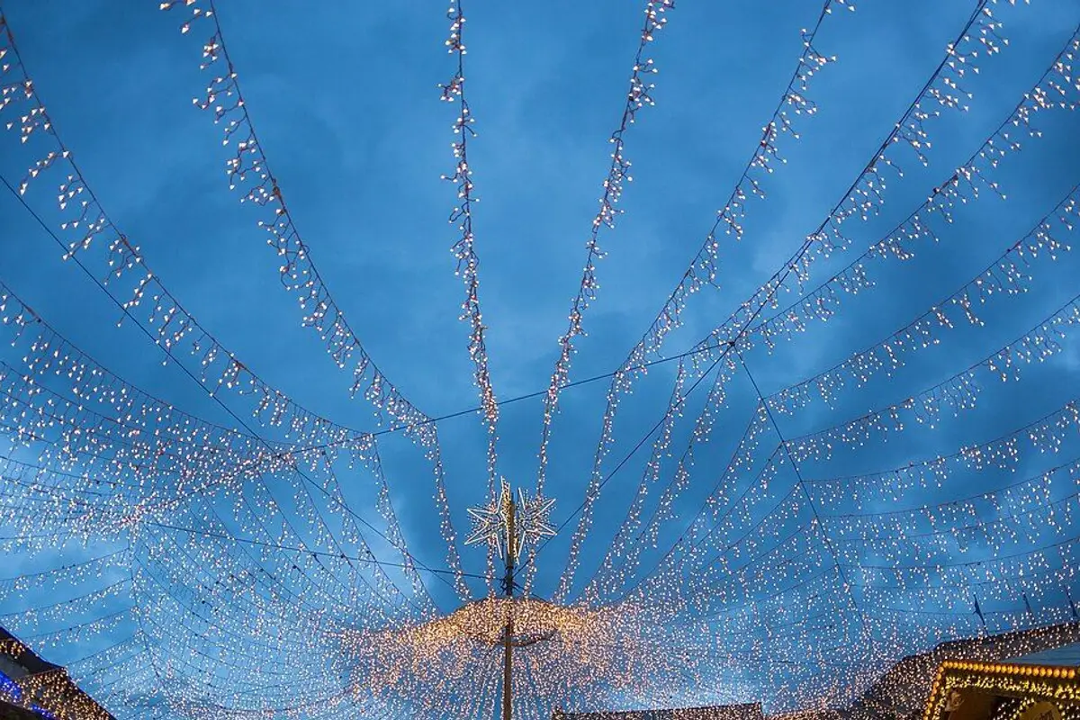 Strings of lights hung over a Christmas market under the evening sky.