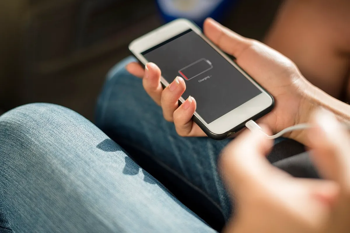 Hands plugging a charging cable into a smartphone with an almost empty battery.