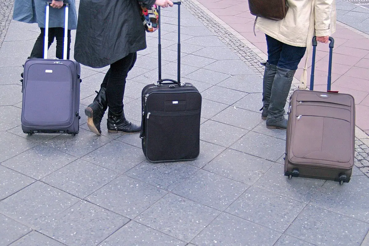 Three wheeled suitcases with handles raised, standing on the pavement outside a station.