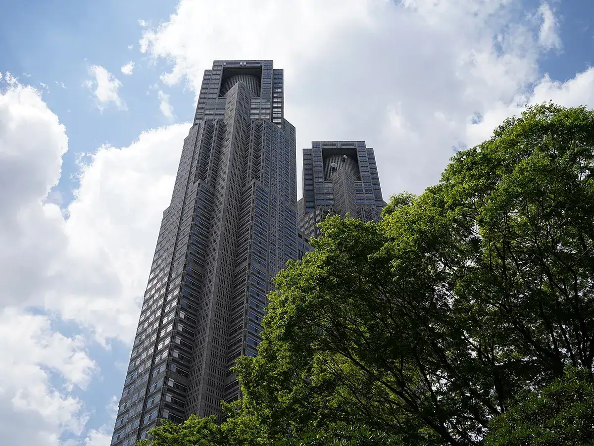 The twin towers of the Tokyo Metropolitan Government Building seen from below, framed by trees.